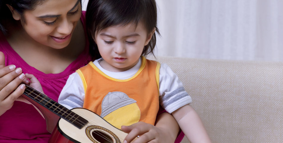 A mom is teaching her daughter to play the guitar